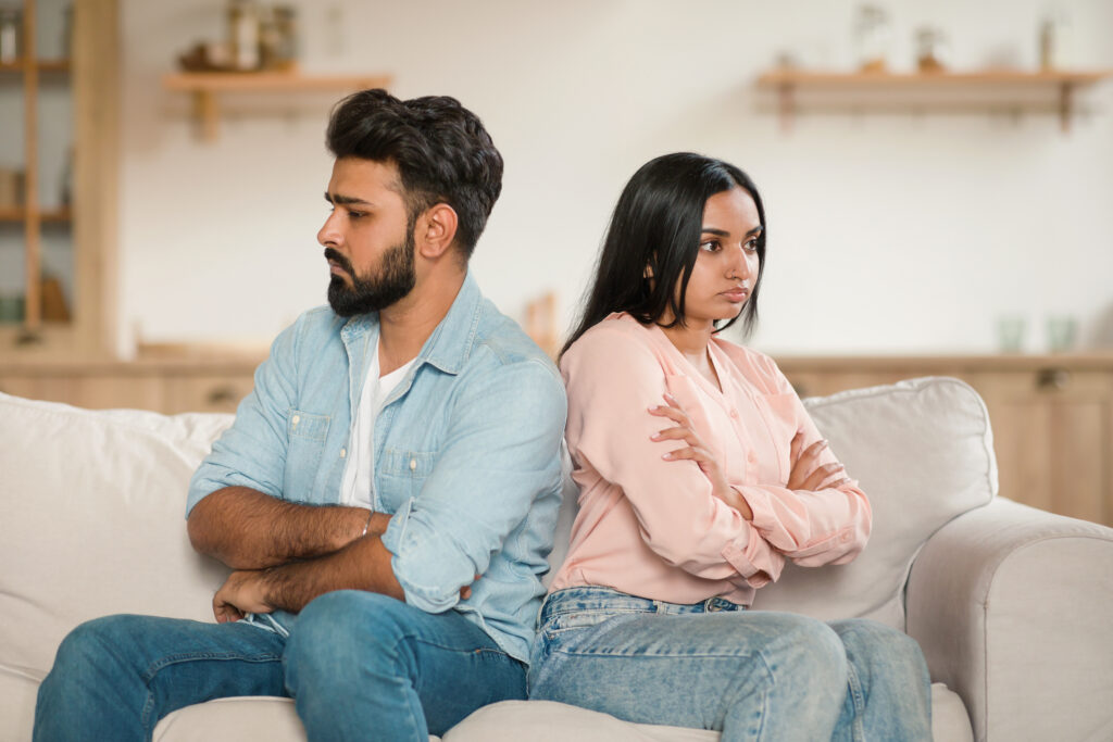 Frustrated couple sitting back-to-back on a couch, displaying emotional dependency and unresolved conflict